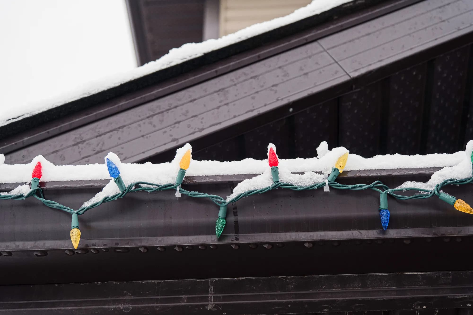 Multicolor holiday lights strung along a snow-dusted roofline gutter